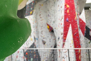 Dekoratives Bild von Boulderwand im Vordergrund mit der Kletterwand im Hintergrund